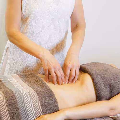 Frau massiert den Bauch einer liegenden Person mit braunem Handtuch.