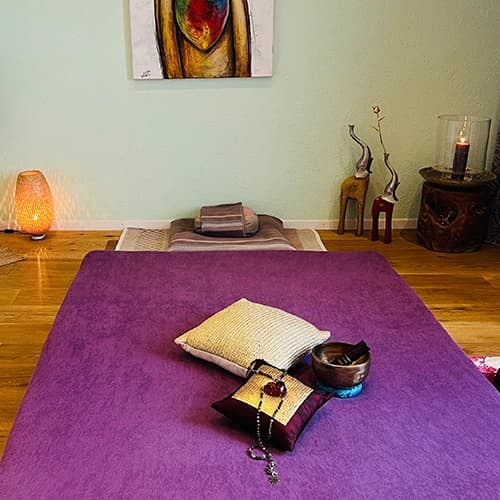 Purple massage mat with cushions, candle and lantern in the warmly lit practice room
