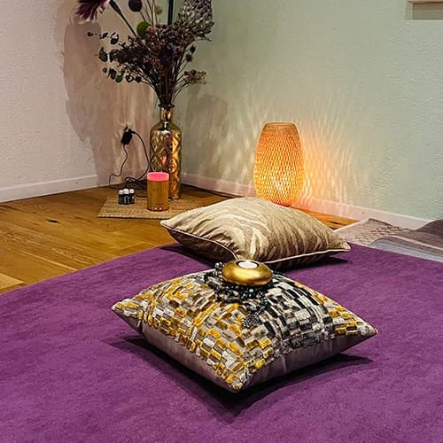 Massage area of the practice with purple mat, golden cushions and warm lamplight