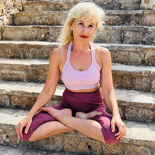 Frau mit blonden Haaren in sportlichem Outfit sitzt im Lotussitz auf Stein-Treppen.