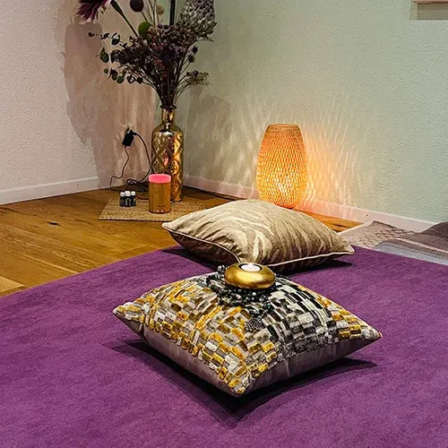 Massage area of the practice with purple mat, golden cushions and warm lamplight